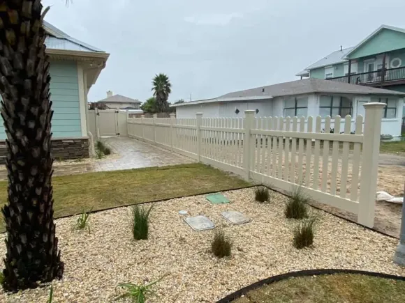 Small gravel front yard with palm tree, white fence, and coastal houses under overcast sky
