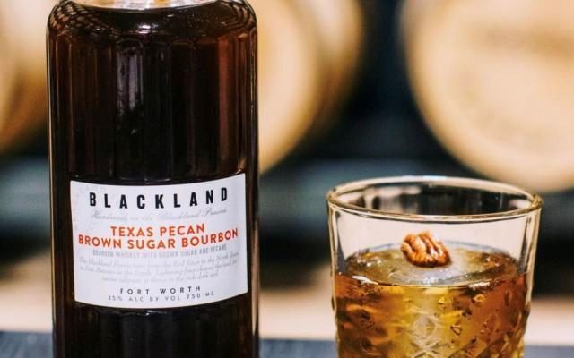 Three bottles of McConnell's Irish whisky on a wooden table, with barrels in the background.