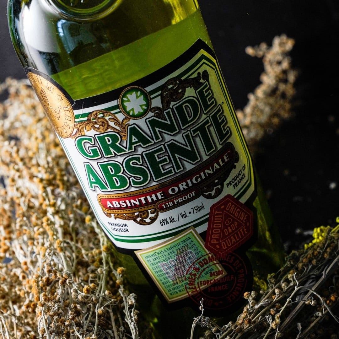 Bottle of Grande Absente absinthe liqueur, green and white label, set on dried herbs.