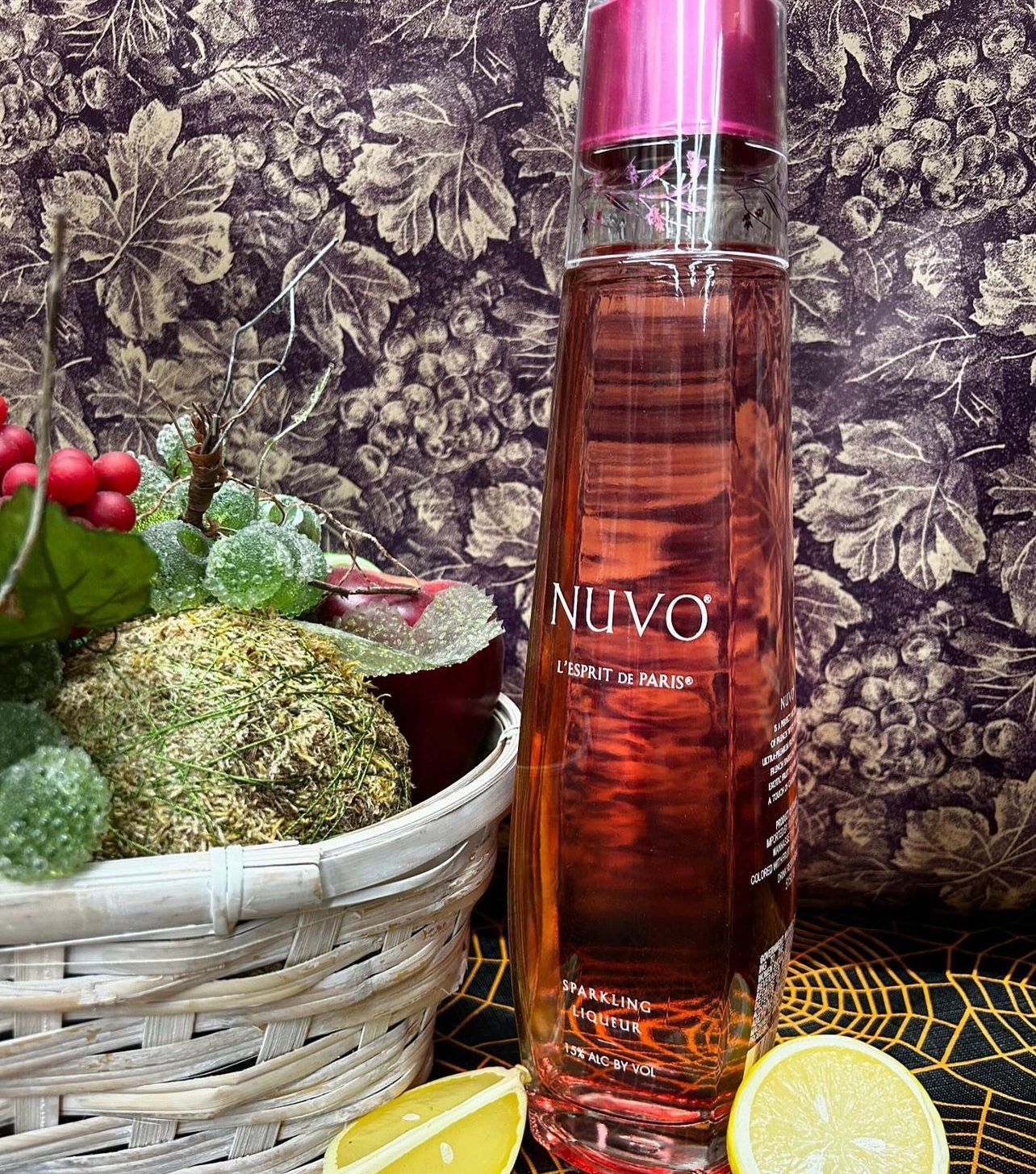 A bottle of perfume is sitting on a table next to a basket of flowers and lemons.