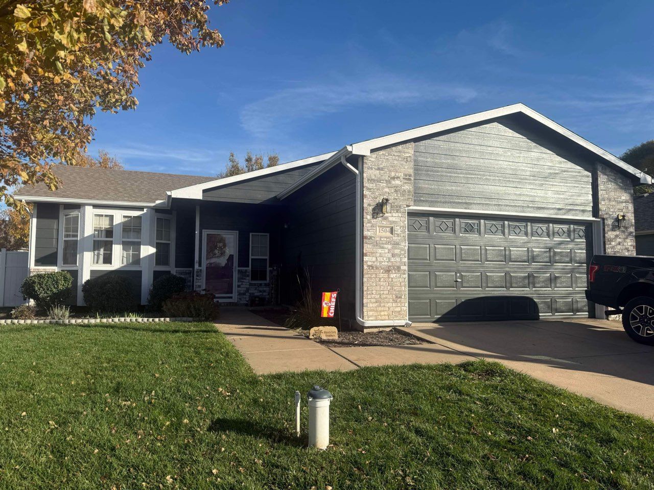 Single-story home with dark gray exterior and brick facade, front yard with grass, blue sky.