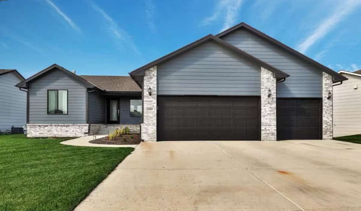 Gray house with stone accents, two-car garage, and green lawn against a blue sky.