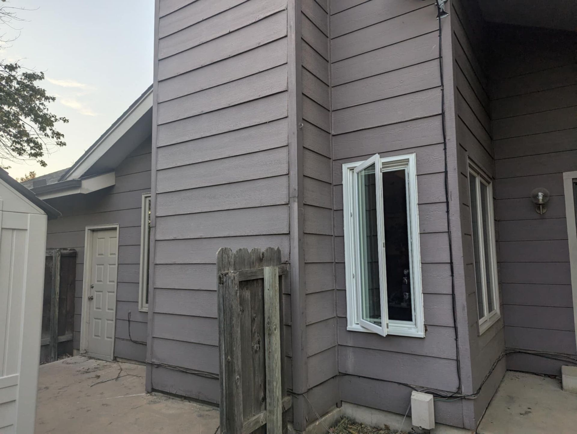 Exterior of a house with gray siding, including a chimney and windows. A fence is in the foreground.