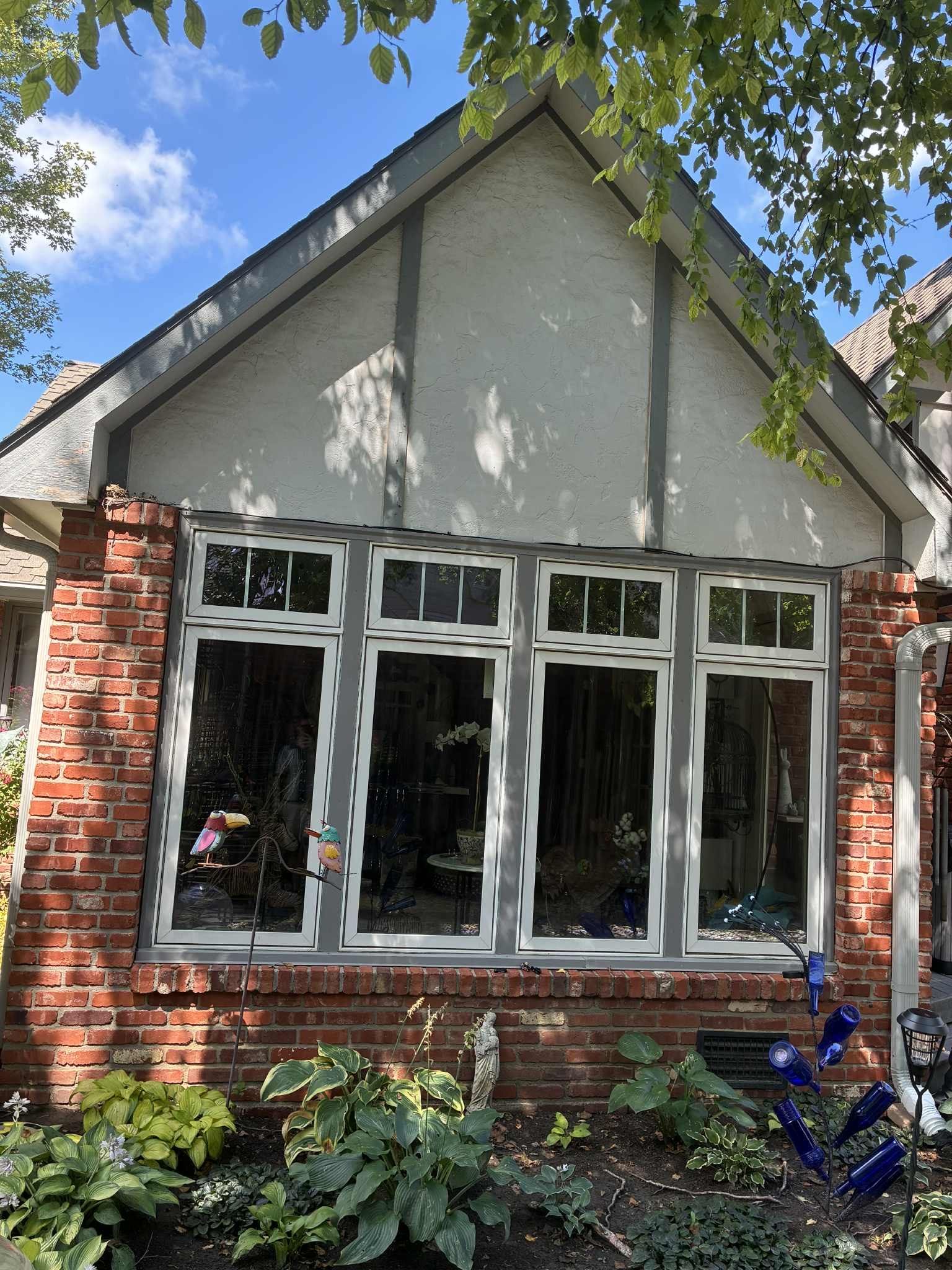 Brick building with large windows, gray trim, stucco gable, and a garden.