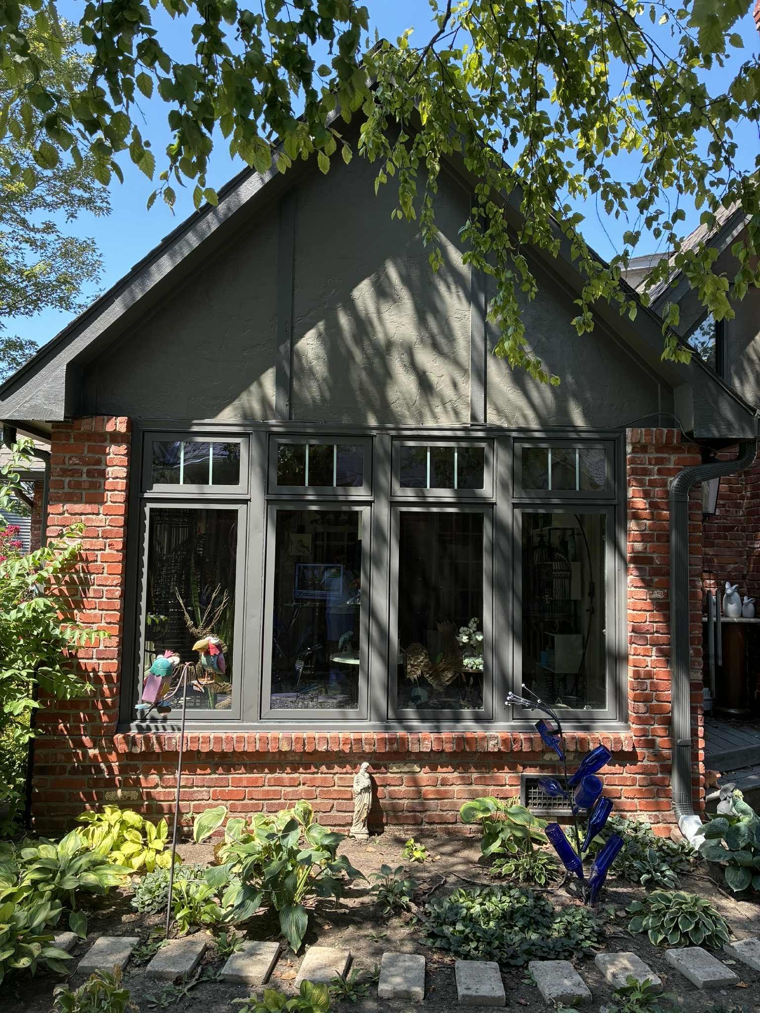 Brick building with dark-framed windows and a gabled roof; lush garden in front.
