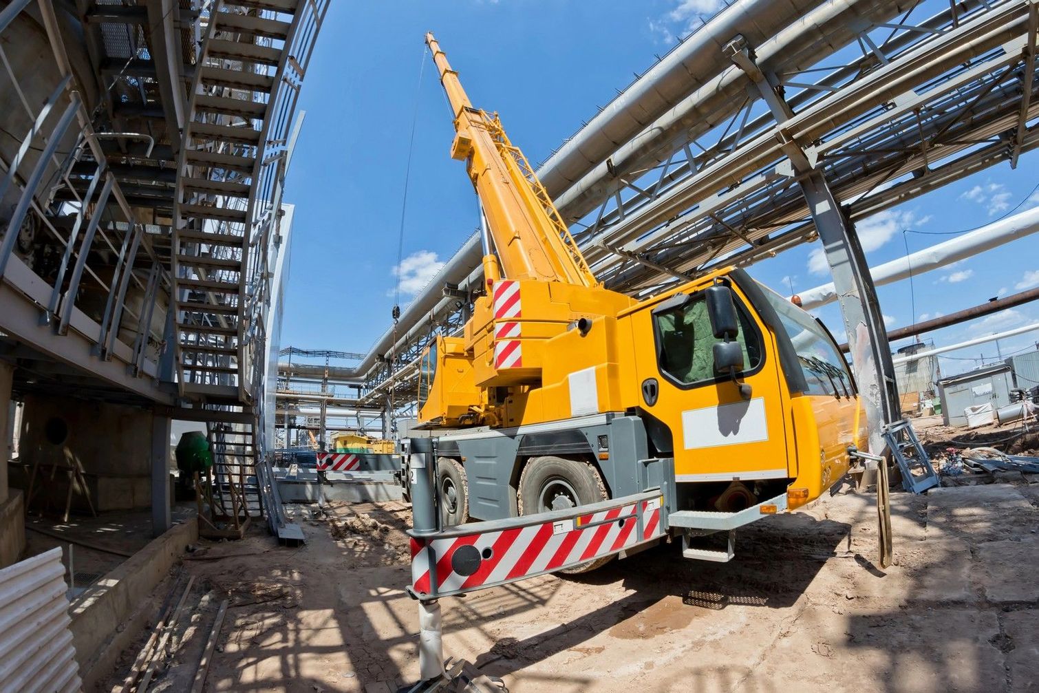 Sotto un cielo azzurro e limpido, in un cantiere industriale, si erge una gru mobile gialla.