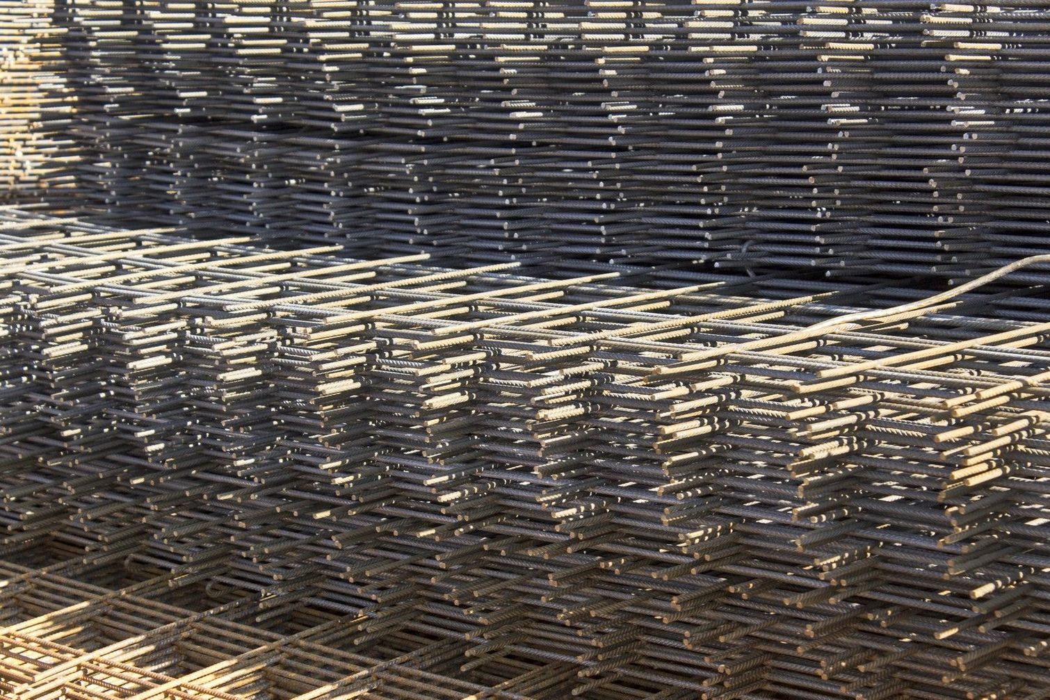 Una grande pila di pannelli rettangolari di rete metallica color argento, impilati uno sull'altro.