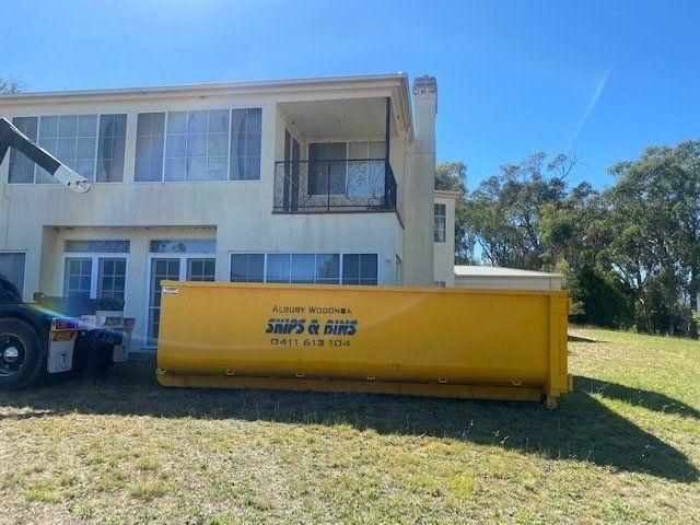 A Large Yellow Dumpster Is Parked In Front Of A Large House — Albury Wodonga Skips & Bins In Baranduda, VIC