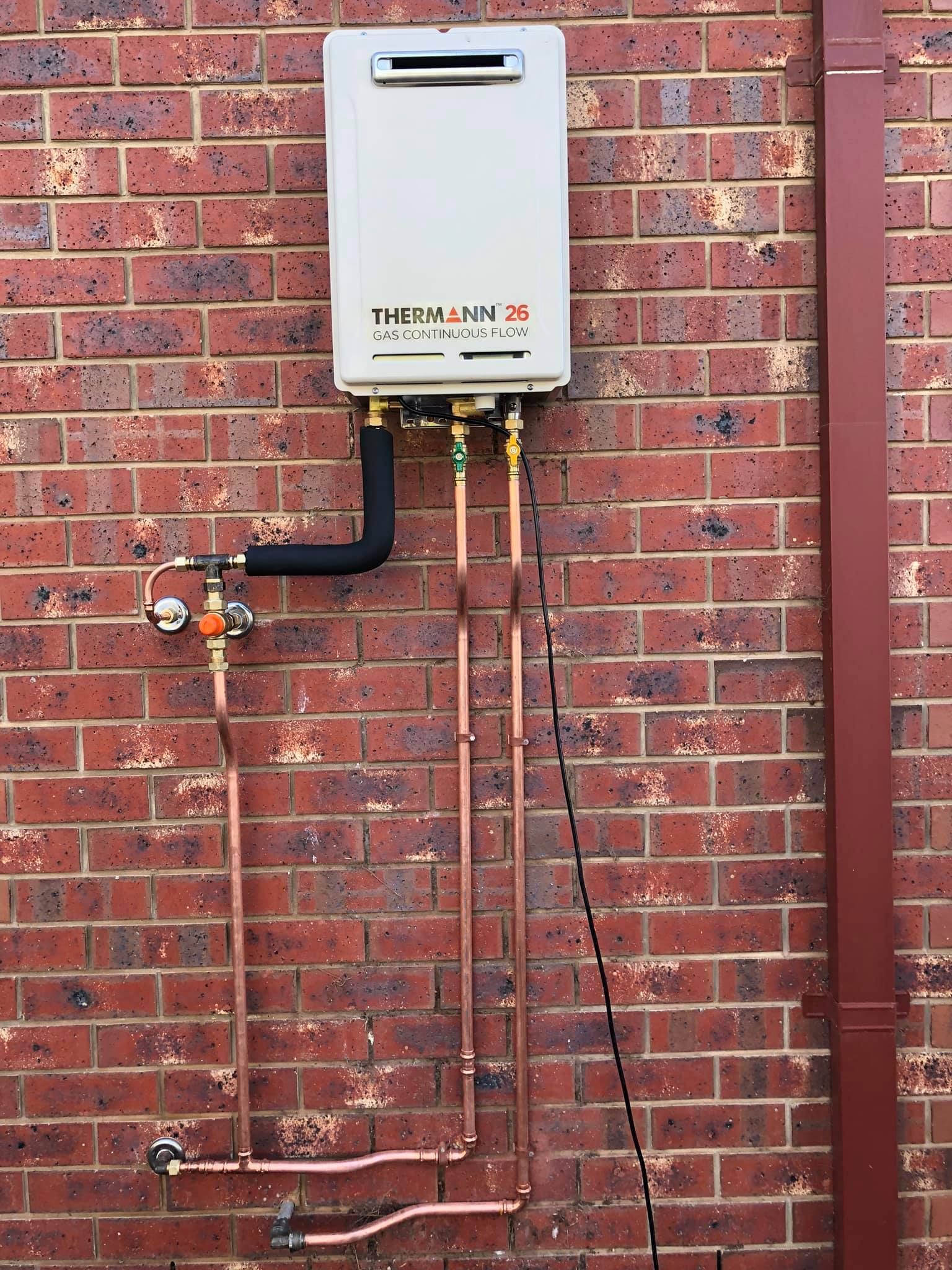 Tankless Water Heater Mounted on a Brick Wall With Copper Pipes — Oxplumb in Coolum Beach, QLD