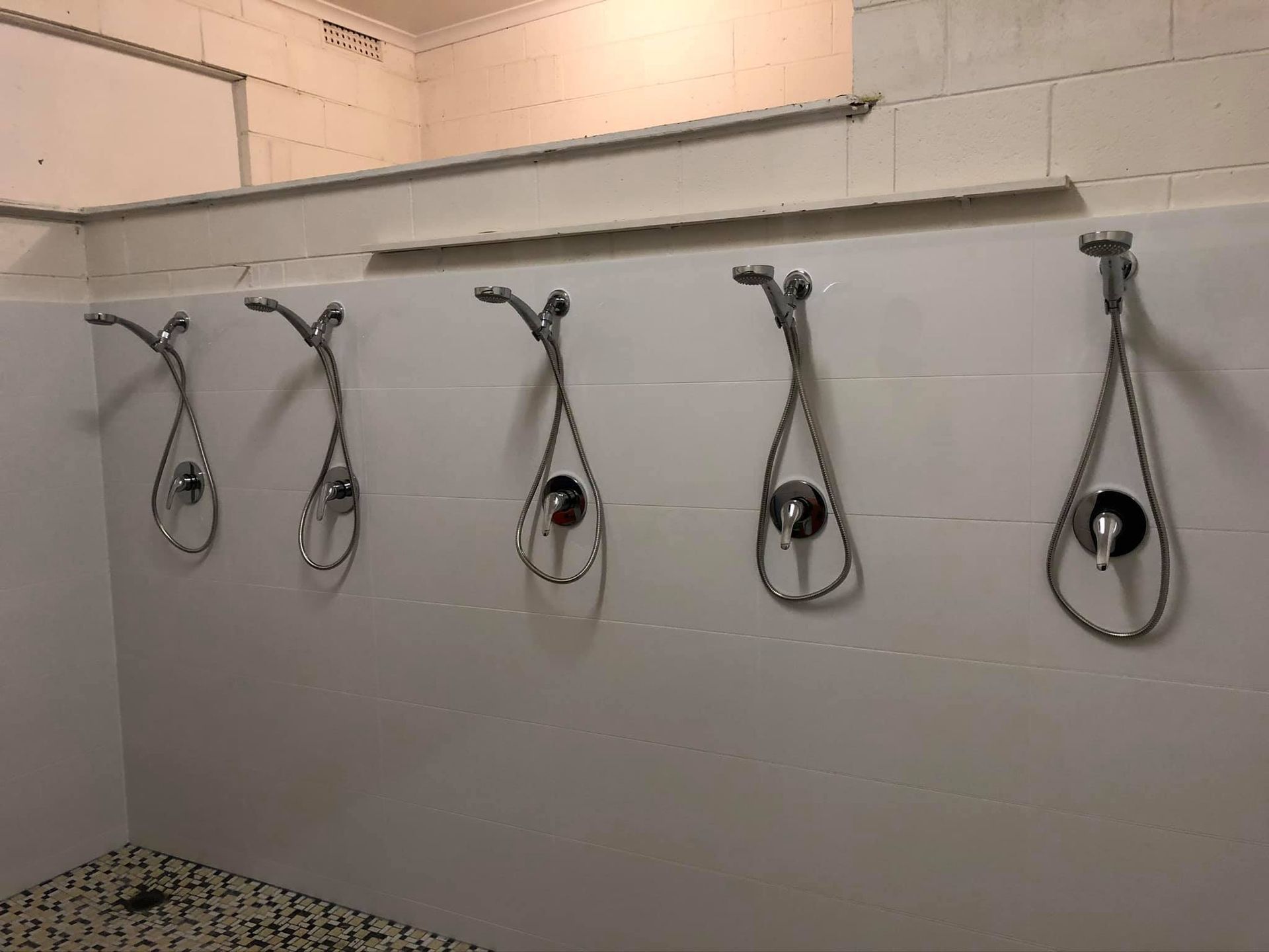 Five Shower Heads With Chrome Fixtures on a Tiled White Wall — Oxplumb in Gympie, QLD