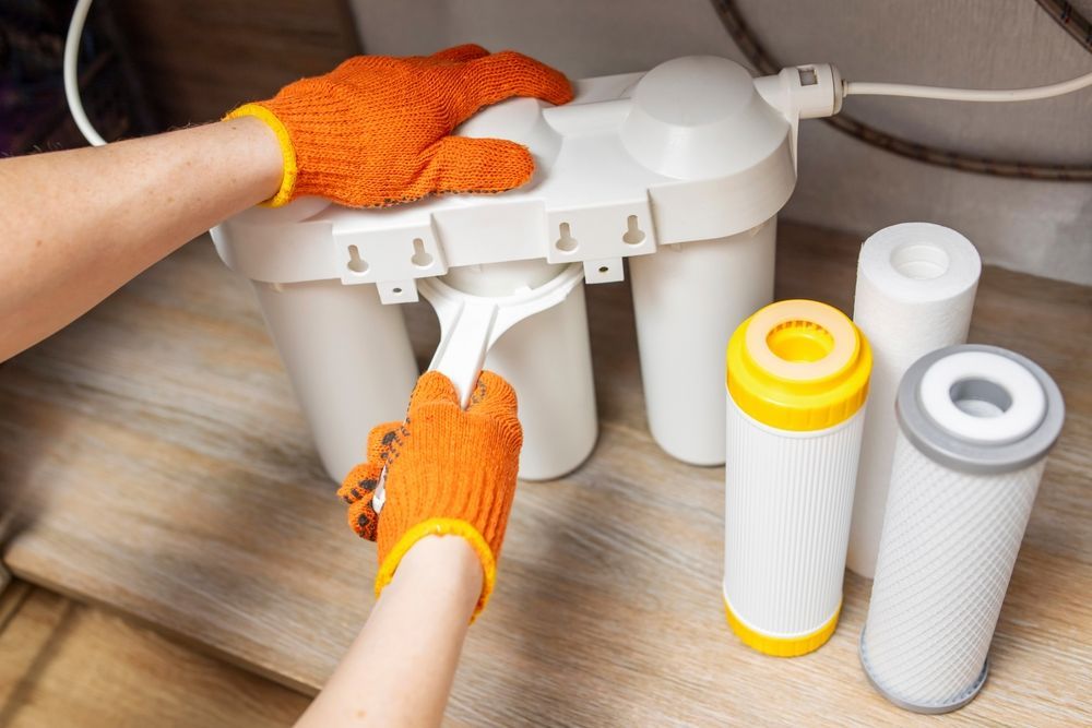 Hands Wearing Orange Gloves Using a Wrench to Change a Water Filter — Oxplumb in Noosa, QLD