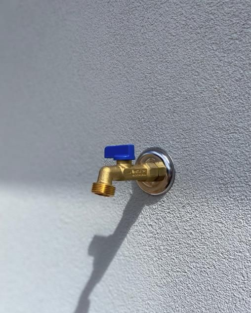 Brass Outdoor Faucet With Blue Handle on a Textured White Wall — Oxplumb in Gympie, QLD