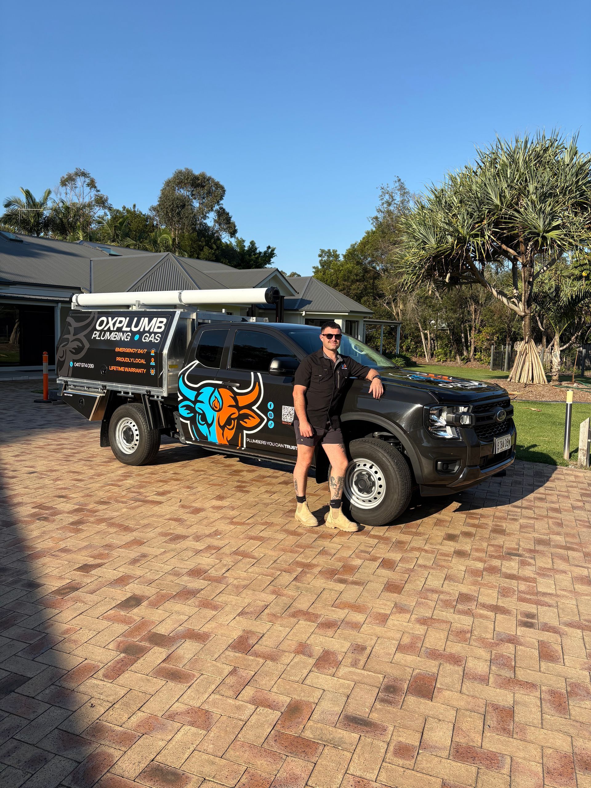 Man Stands Next to a Black Work Truck in a Driveway — Oxplumb in Coolum Beach, QLD