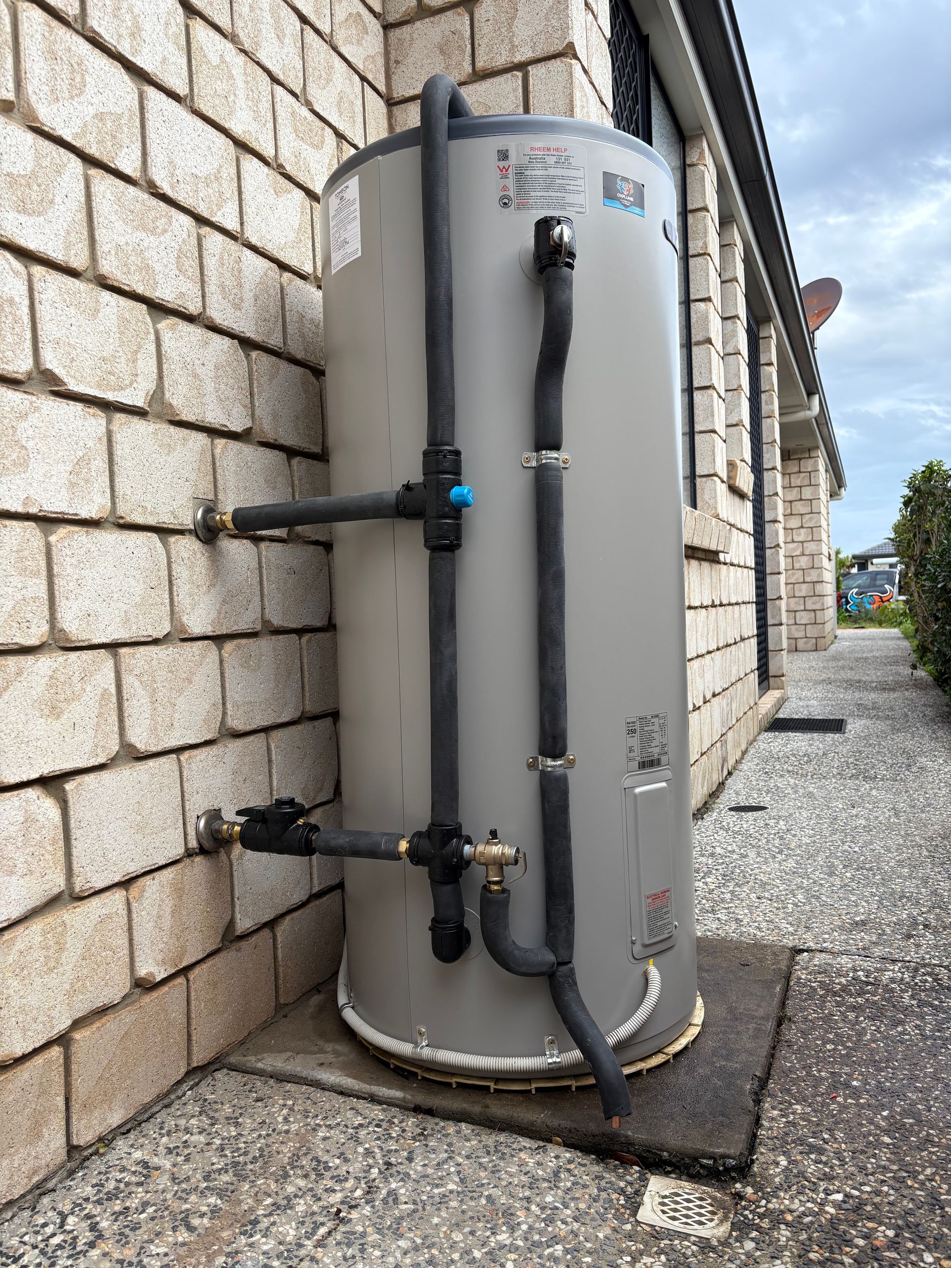 A Tall, Cylindrical Hot Water Tank Mounted on a Brick Wall — Oxplumb in Coolum Beach, QLD