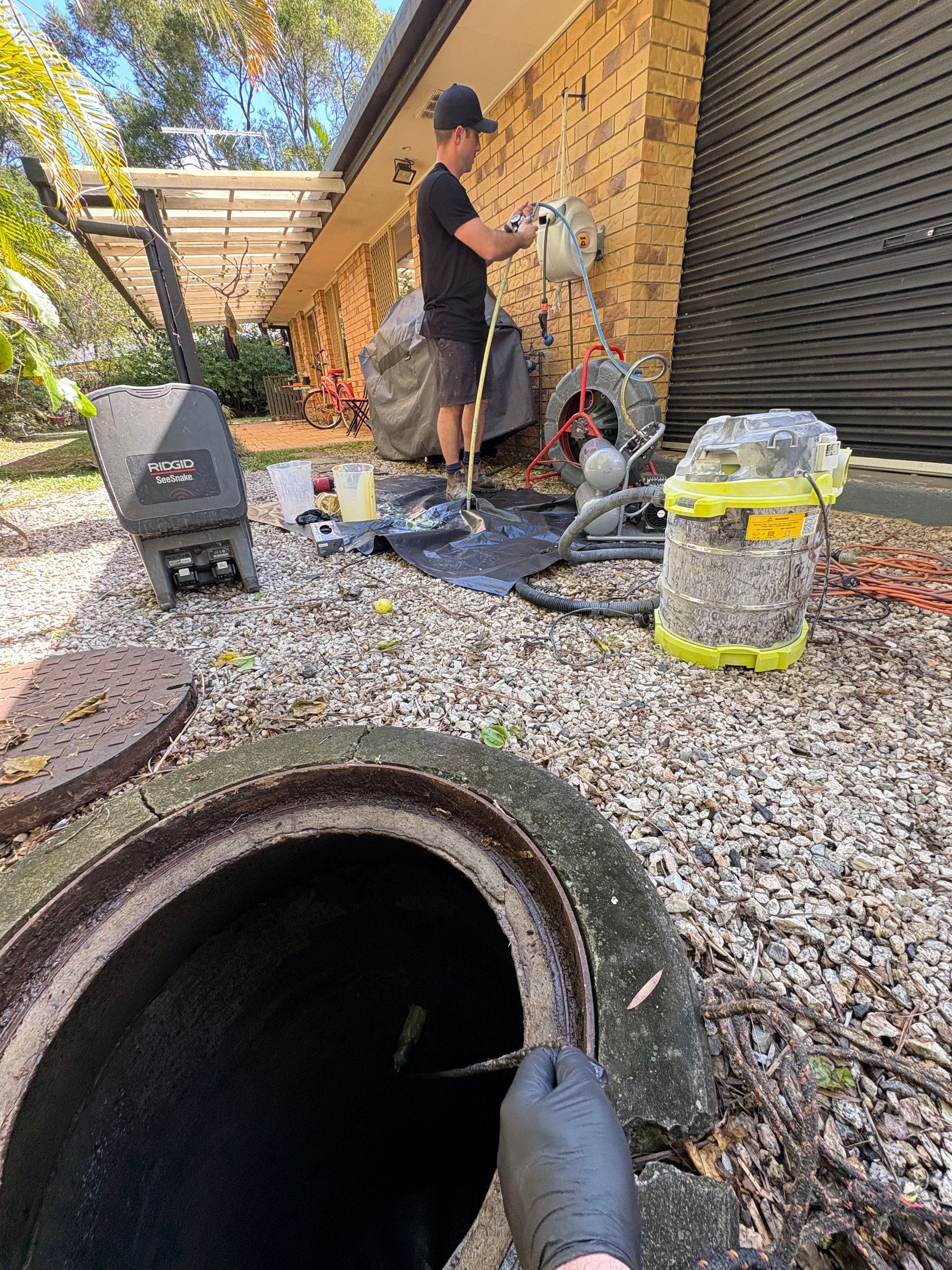 Man Cleaning a Sewage Drain in a Yard; Open Manhole in Foreground — Oxplumb in Coolum Beach, QLD