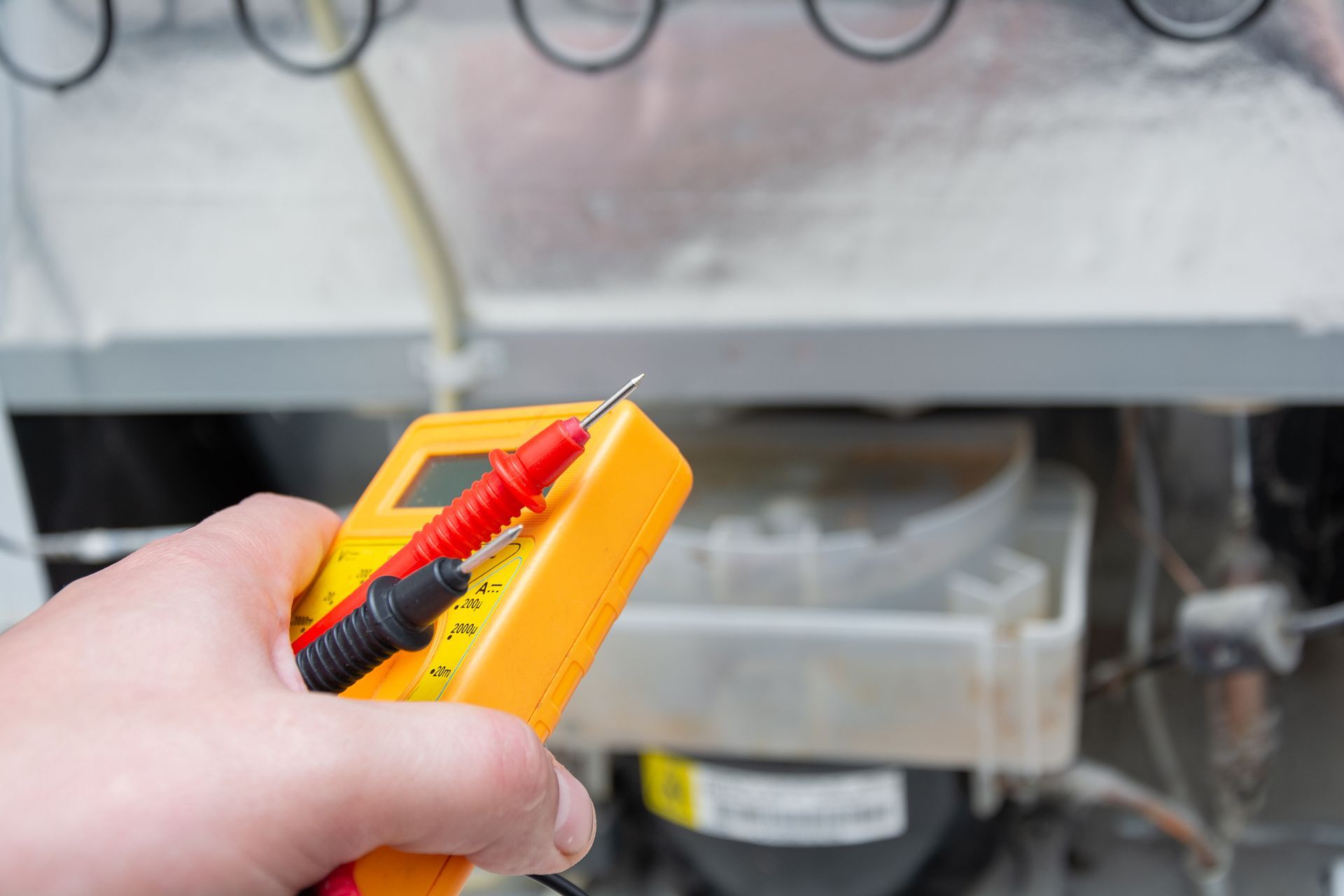 A Person Holds Multimeter While Inspecting the Back of An Appliance Compressor — Central Coast Washing Machines & Refrigerator Repairs in Gosford, NSW