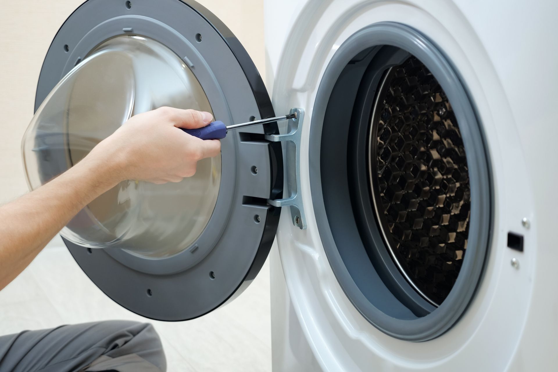 A Person Uses a Screwdriver to Tighten a Screw on the Door Hinge — Central Coast Washing Machines & Refrigerator Repairs in San Remo, NSW