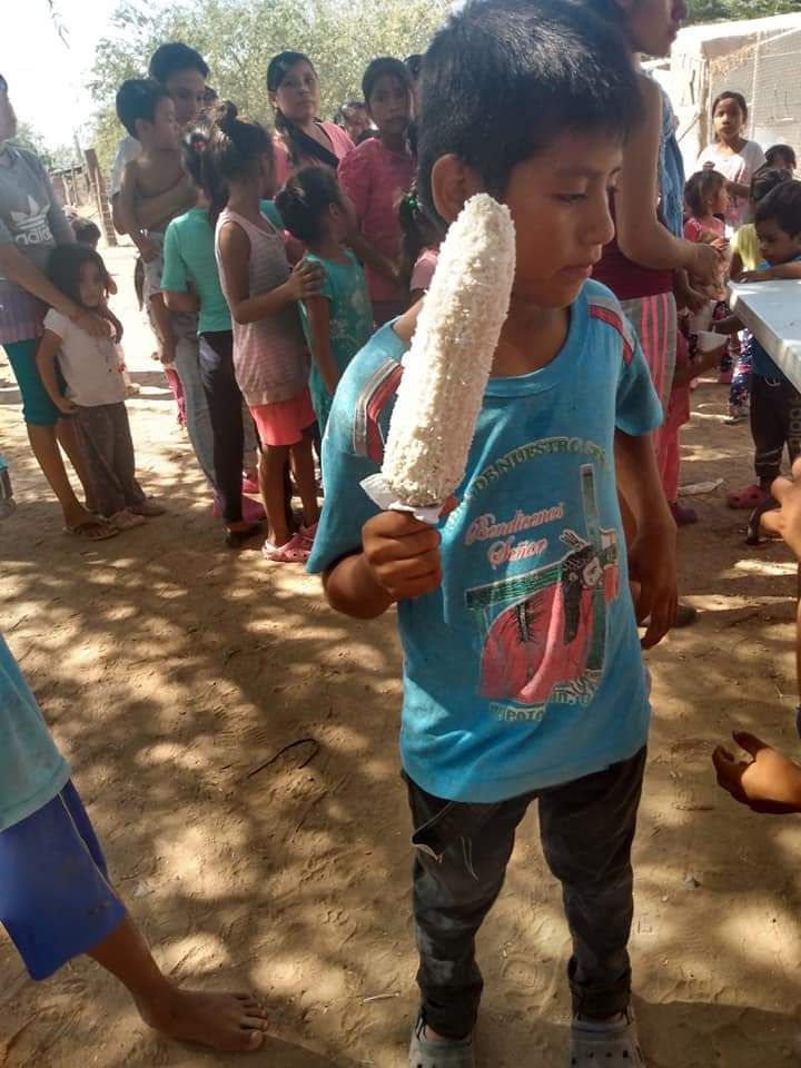 A young boy is holding a corn on the cob in front of a crowd of people.