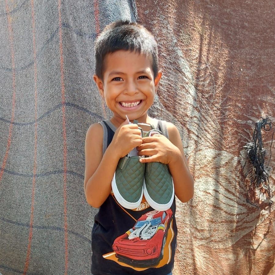 A young boy is holding a pair of shoes and smiling