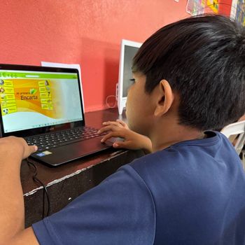 A young boy is using a laptop with the word escuela on the screen