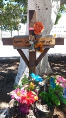 A wooden cross is surrounded by flowers and a tree.