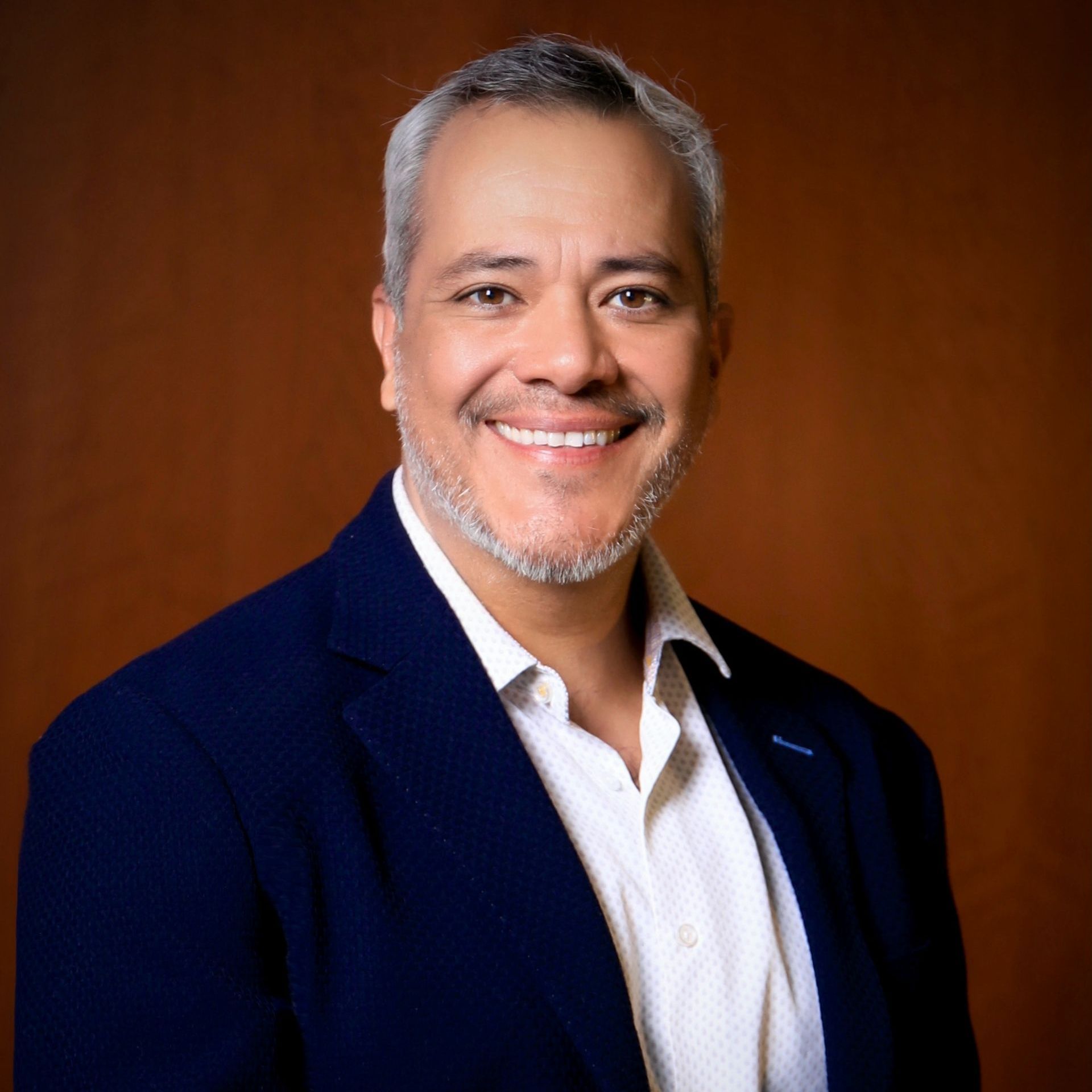 A man with a beard wearing a blue jacket and white shirt is smiling for the camera.