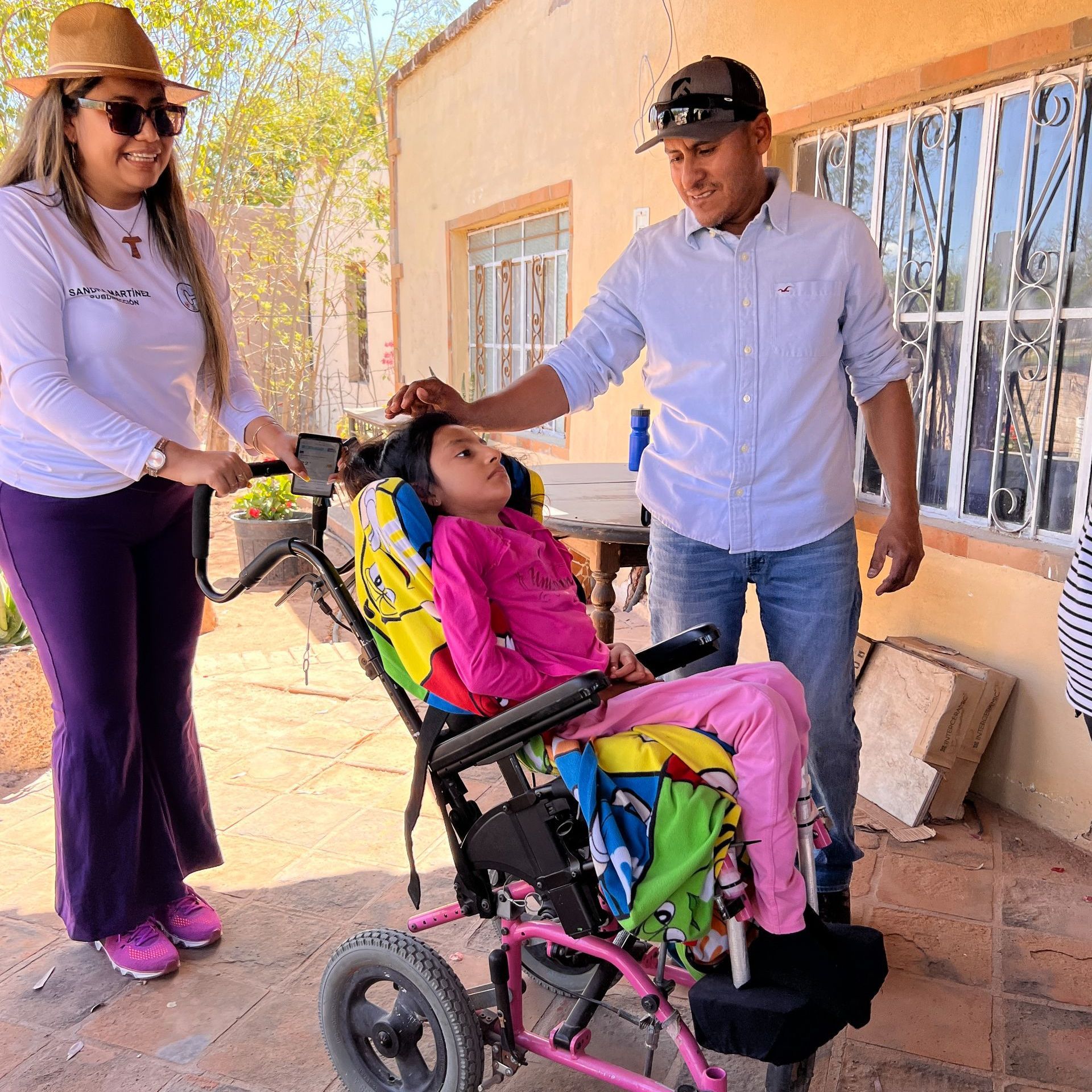 A girl in a wheelchair is being helped by a man and woman