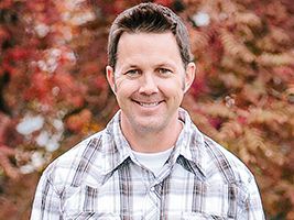 A man in a plaid shirt is smiling in front of a tree.