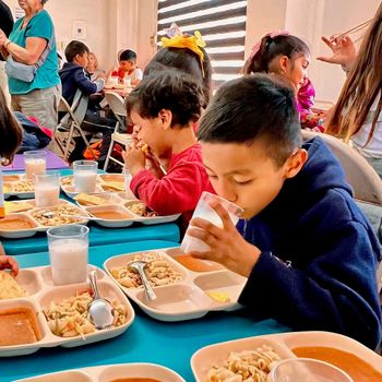 A group of children are sitting at a table eating food and drinking milk.