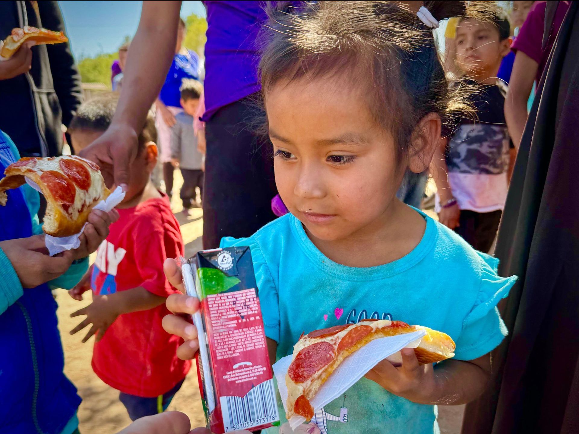 A little girl is holding a slice of pizza and a carton of milk.