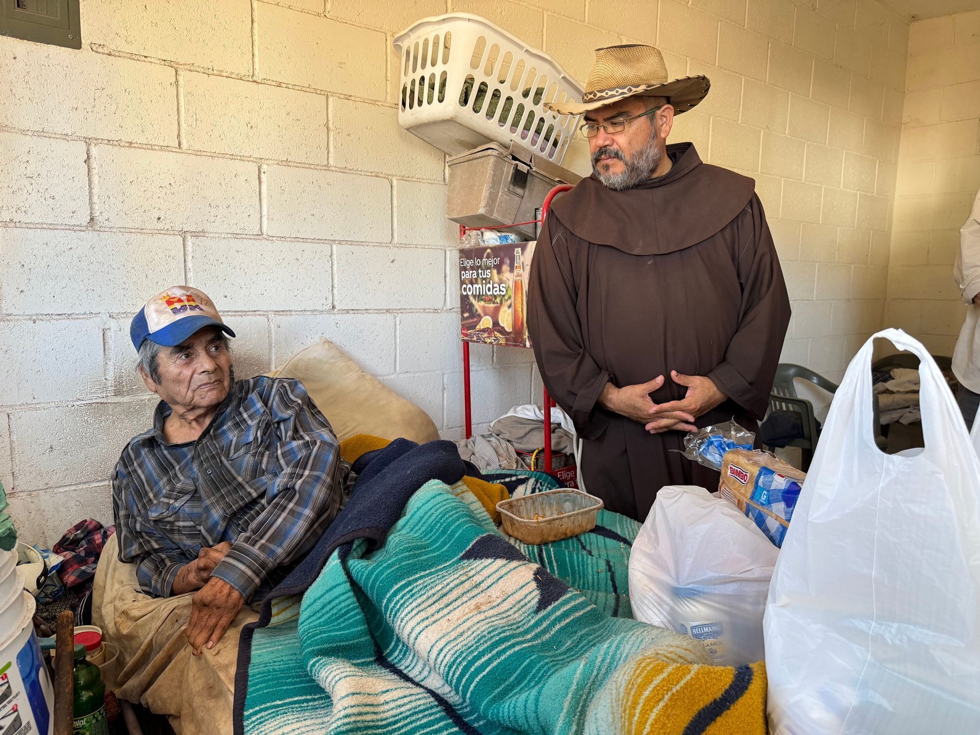 A man in a cowboy hat is standing next to a man in a bed.