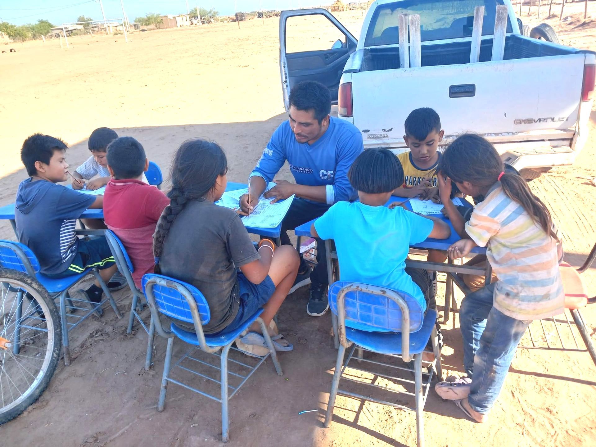 A group of children are sitting around a table in front of a truck.