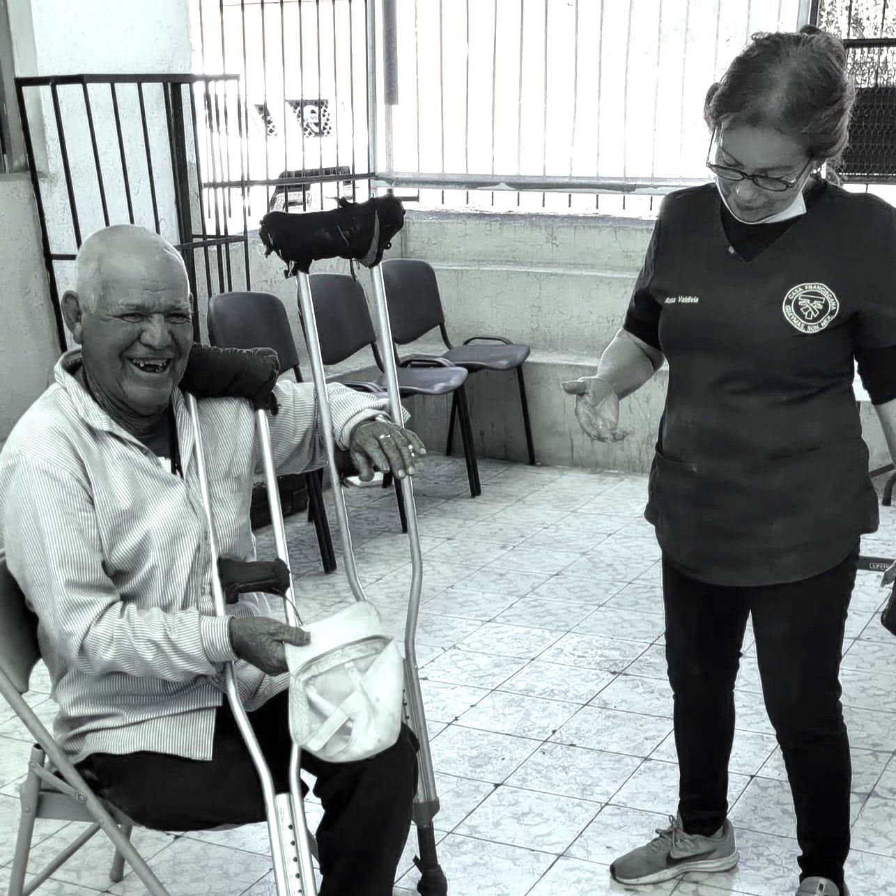 A man with crutches is sitting in a chair next to a woman.