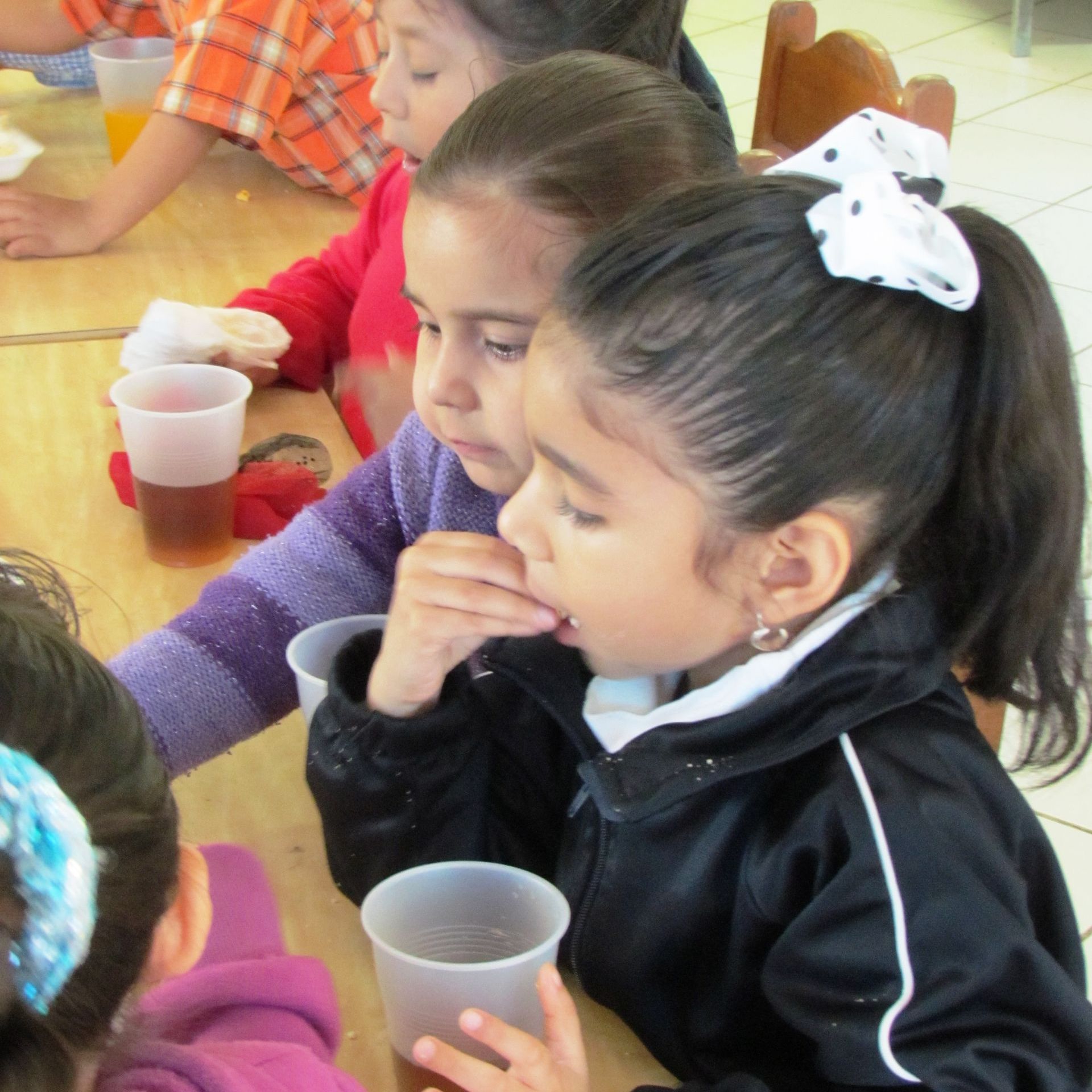 A group of young girls are sitting at a table drinking from plastic cups