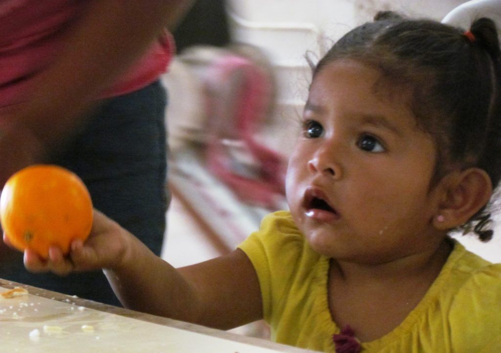 A little girl in a yellow shirt is holding an orange