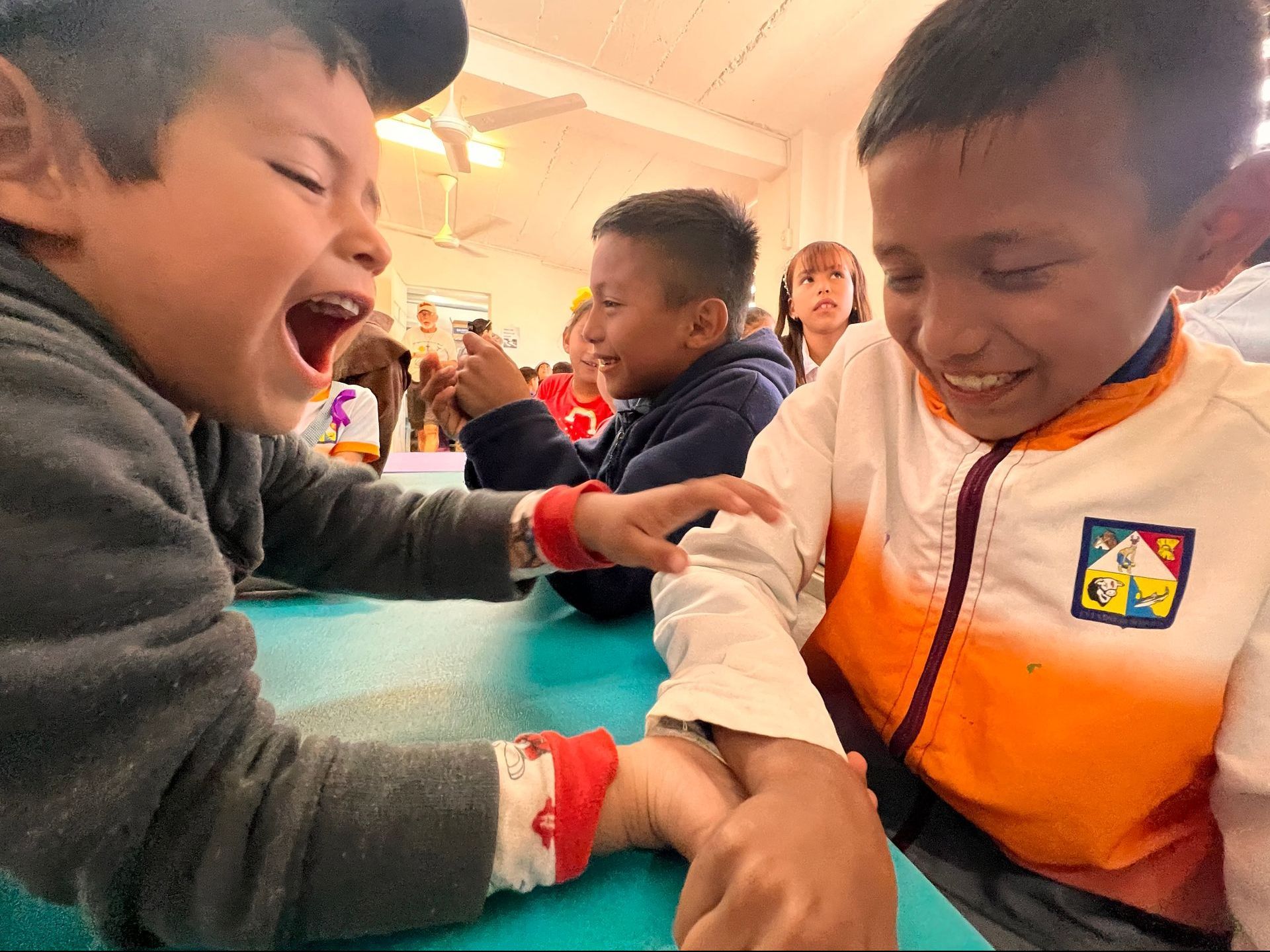 Two young boys are sitting at a table holding hands and laughing.