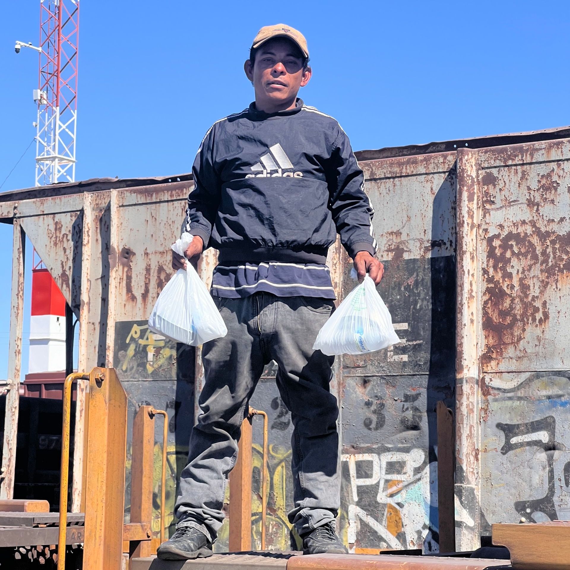 A man wearing an adidas shirt is holding two bags