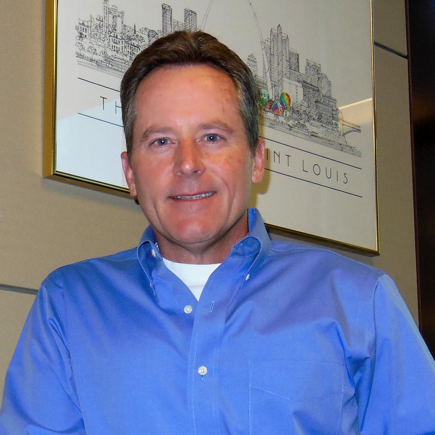 A man in a blue shirt is smiling in front of a picture of st. louis