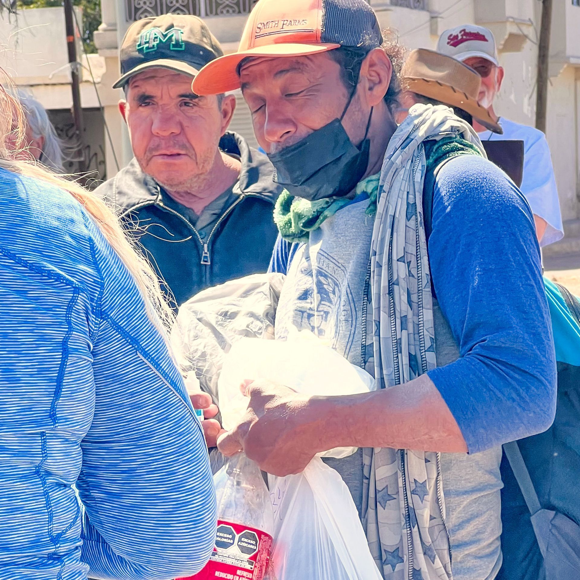 A man wearing a mask and a hat is holding a bag of food.