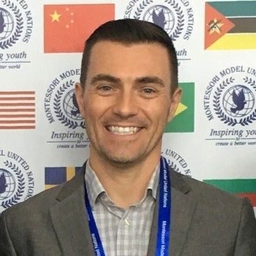 A man in a suit is smiling in front of a wall with flags on it.