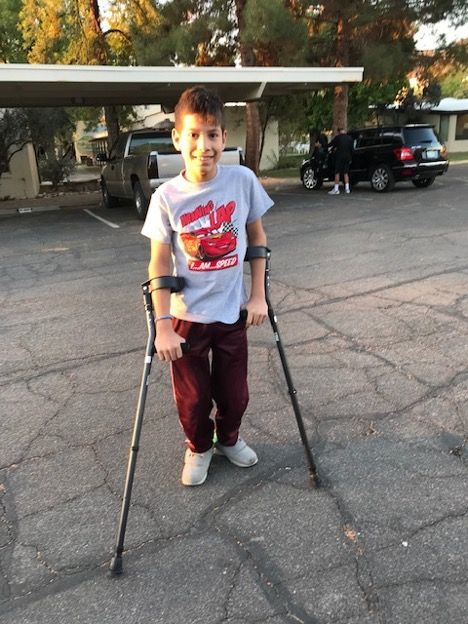 A young boy with crutches in a parking lot