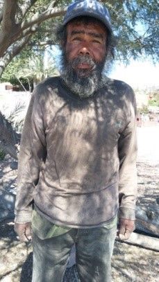 A man with a beard and a hat is standing under a tree.