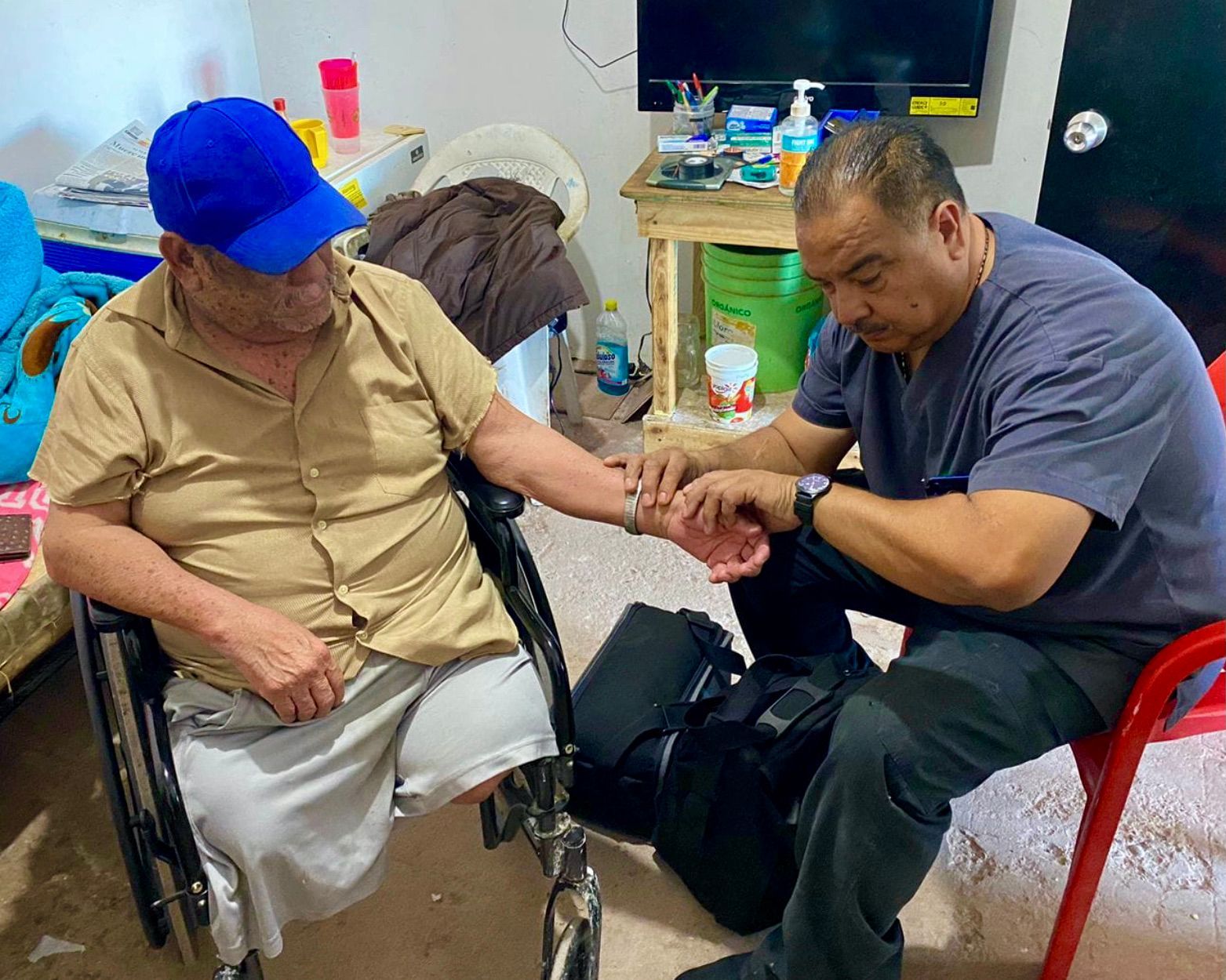 A man in a blue hat is sitting next to a man in a wheelchair.