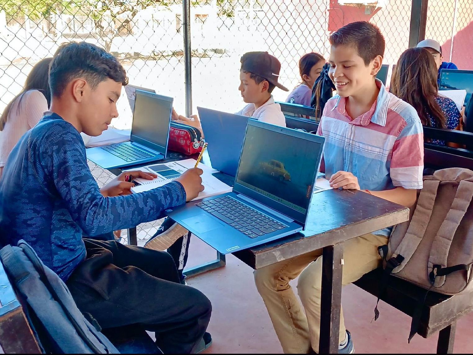 A group of children are sitting at tables with laptops.