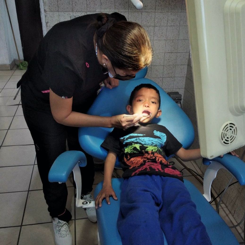 A young boy is laying in a dental chair while a woman examines his teeth