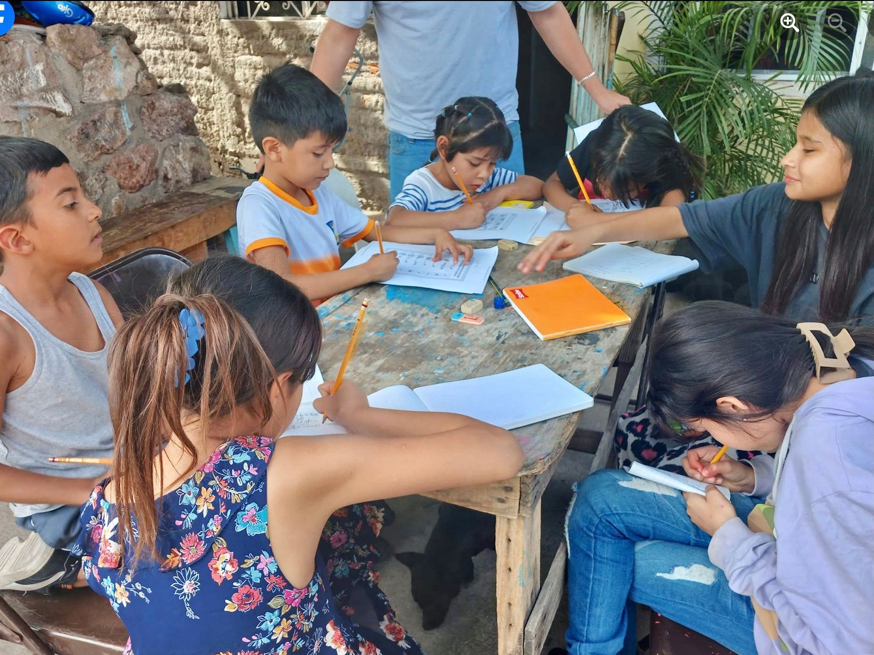 A group of children are sitting around a table writing in notebooks