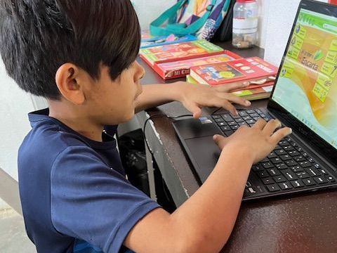 A young boy is sitting at a desk using a laptop computer.