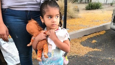 A little girl is holding a doll in her arms while standing next to a woman.