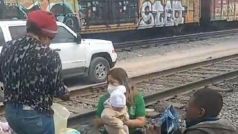 A woman is holding a baby on the train tracks.