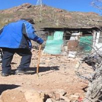 A man in a blue jacket is walking in the dirt with a cane.